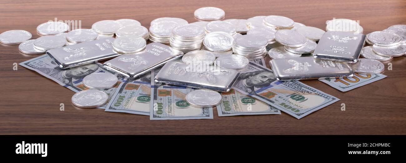 Closeup of Silver bars and silver coins and 100 dollar bills on wooden table Stock Photo