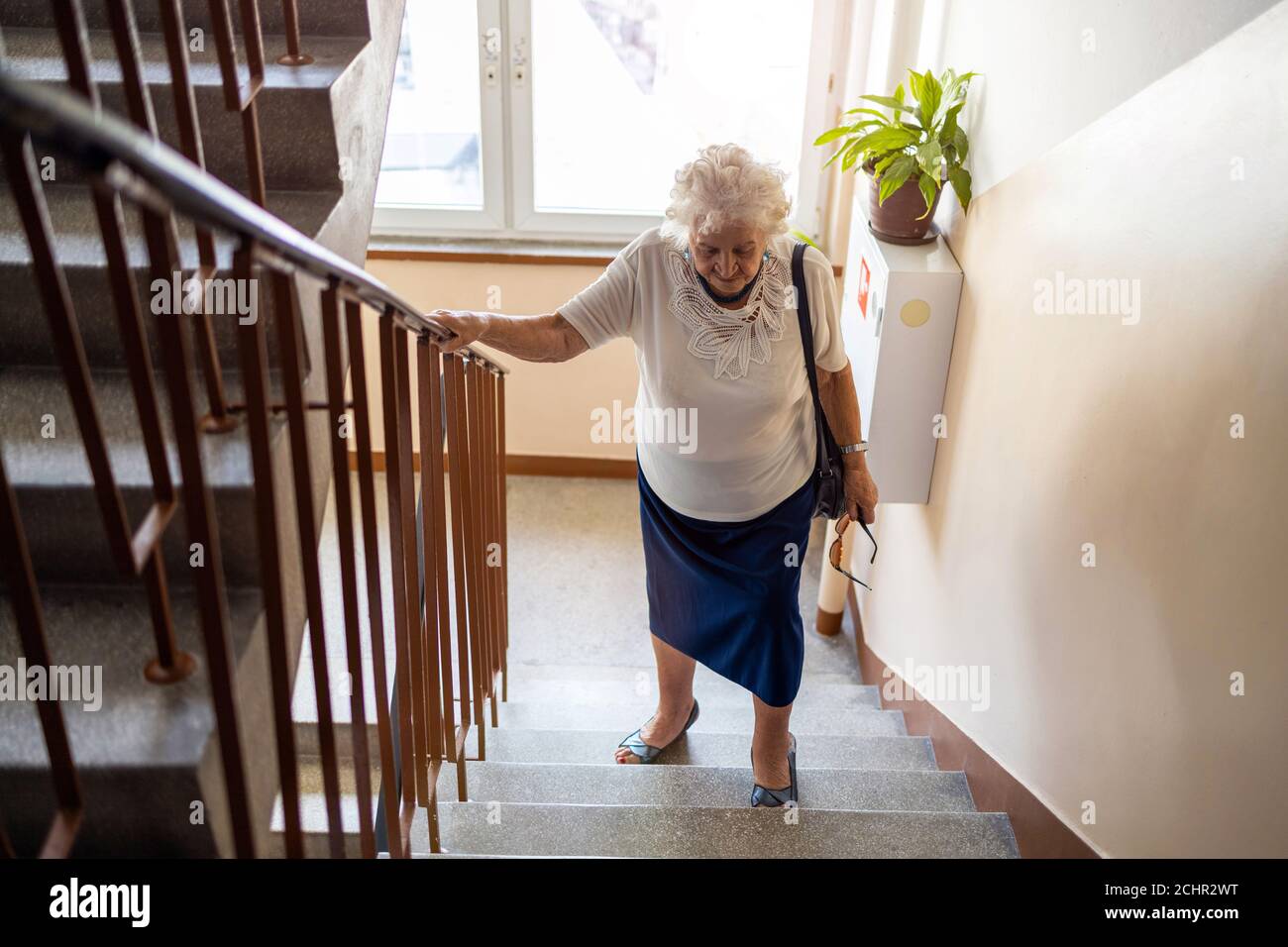 Senior woman climbing staircase with difficulty Stock Photo