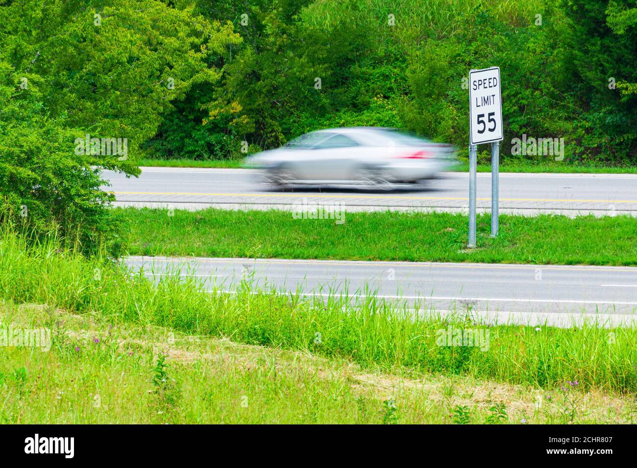 Horizontal shot of a speeding car streaking by a speed limit sign.  Blurring shows motion. Stock Photo