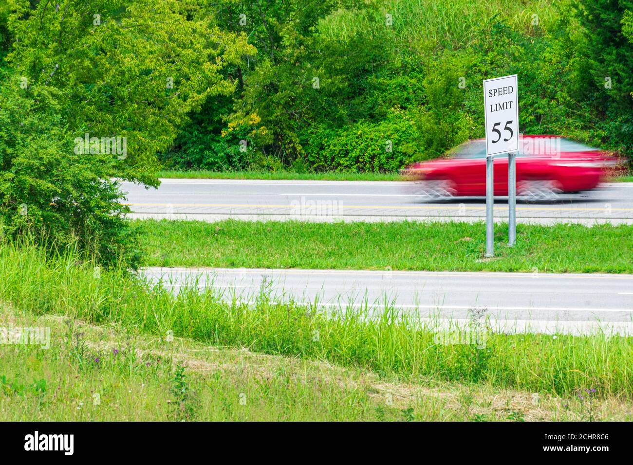 Horizontal shot of a speeding red car streaking by a speed limit sign.  Blurring shows motion. Stock Photo