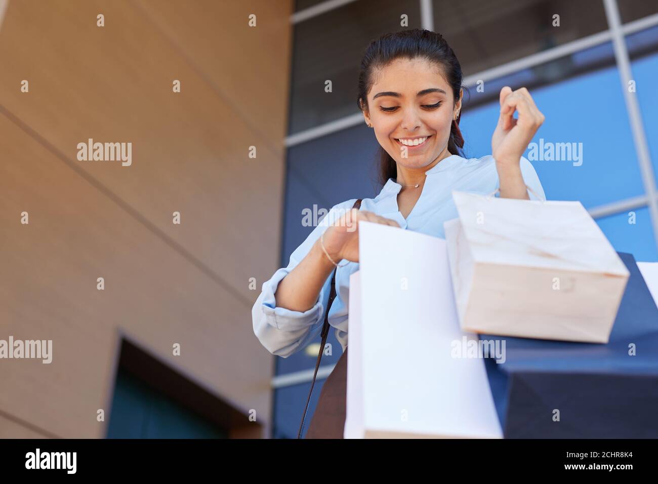Low angle portrait of happy young woman looking into shopping bag and smiling while leaving mall with purchases, copy space Stock Photo