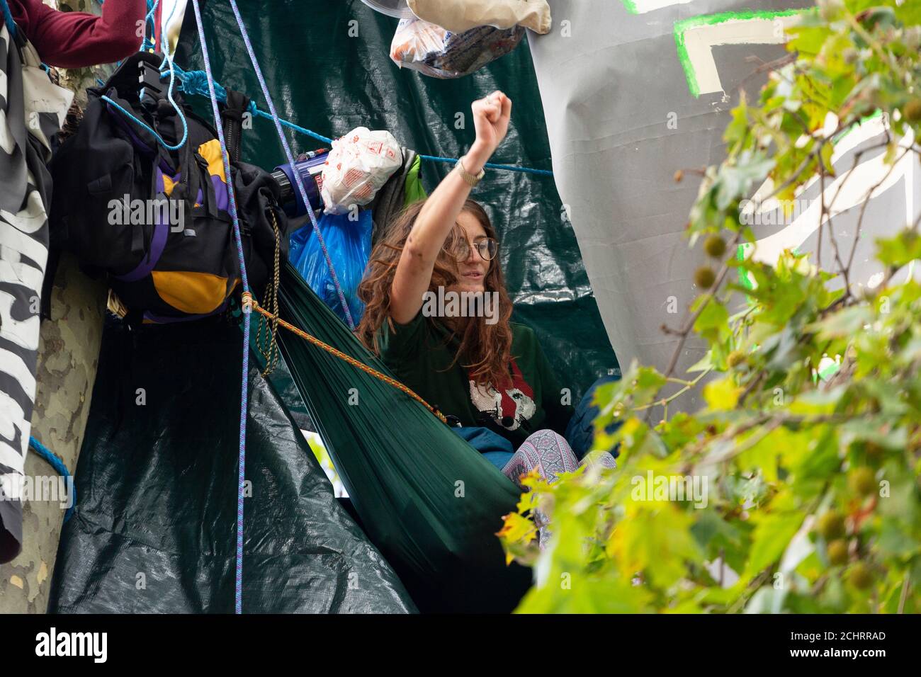 Protester raises her fist from hammock during HS2 Rebellion tree occupation, Parliament Square, London, 5 September 2020 Stock Photo