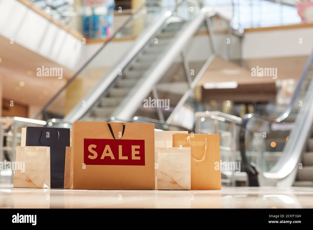 Warm toned image of paper shopping bags on floor in mall with escalator in background, sale concept, copy space Stock Photo