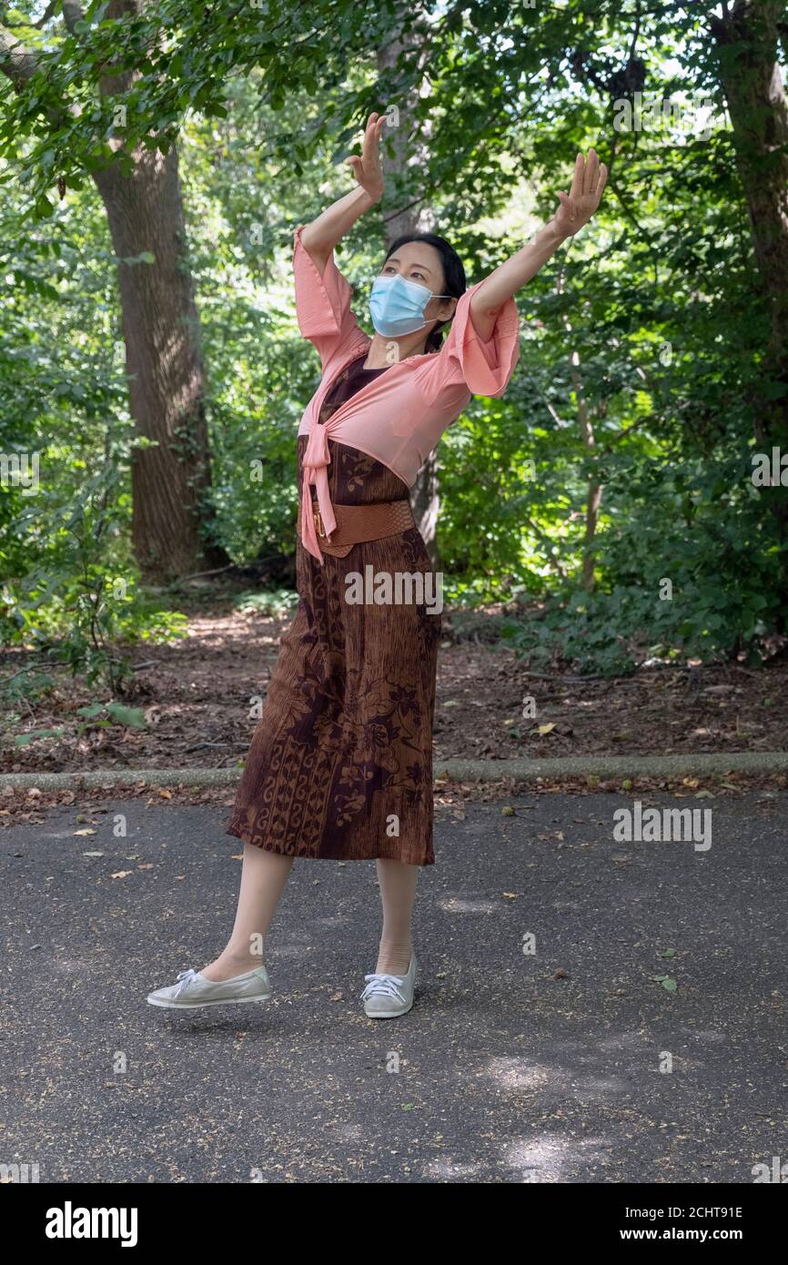 Surrounded by trees and foliage, a graceful Chinese American dancer dances to traditional folk music. I a park in Queens, New York City Stock Photo