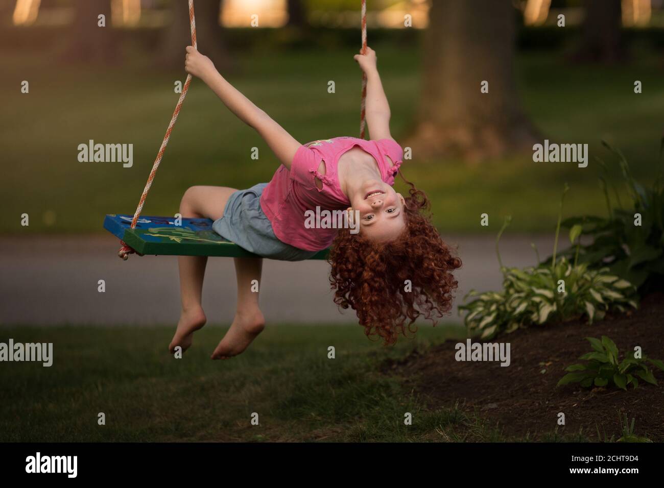 Young red headed girl hanging upside on a tree swing Stock Photo