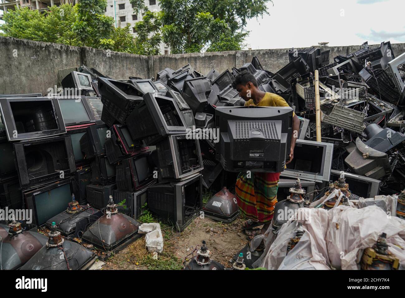 A man is seen sorting TVs for recycle at a TV recycling scrap yard in