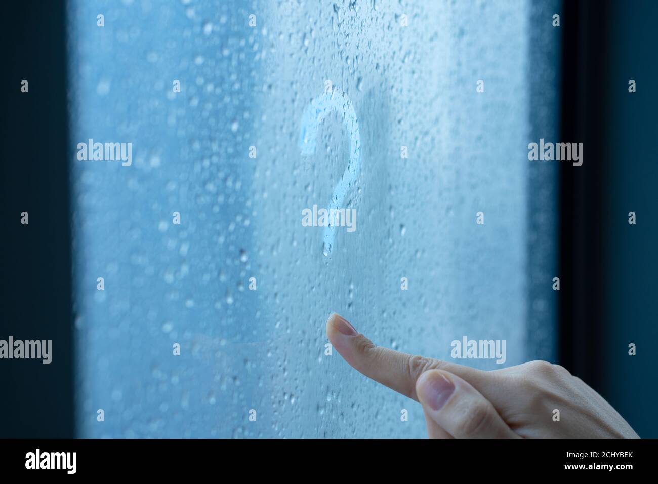 Female hand draws a question mark on a foggy window during the rain. A glass in drops of water Stock Photo