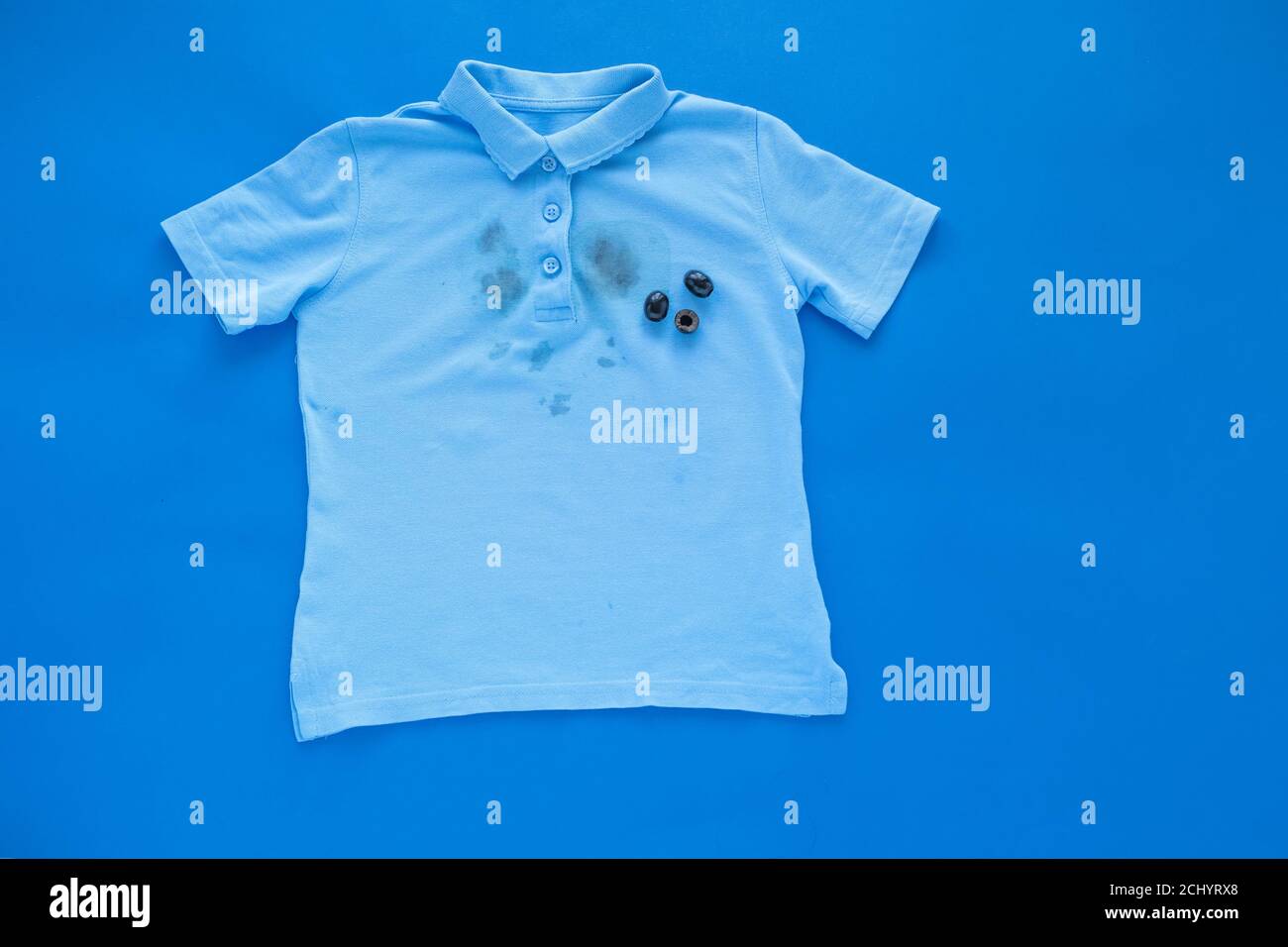 dirty stain of black olives on a t-shirt, isolated on a blue background Stock Photo