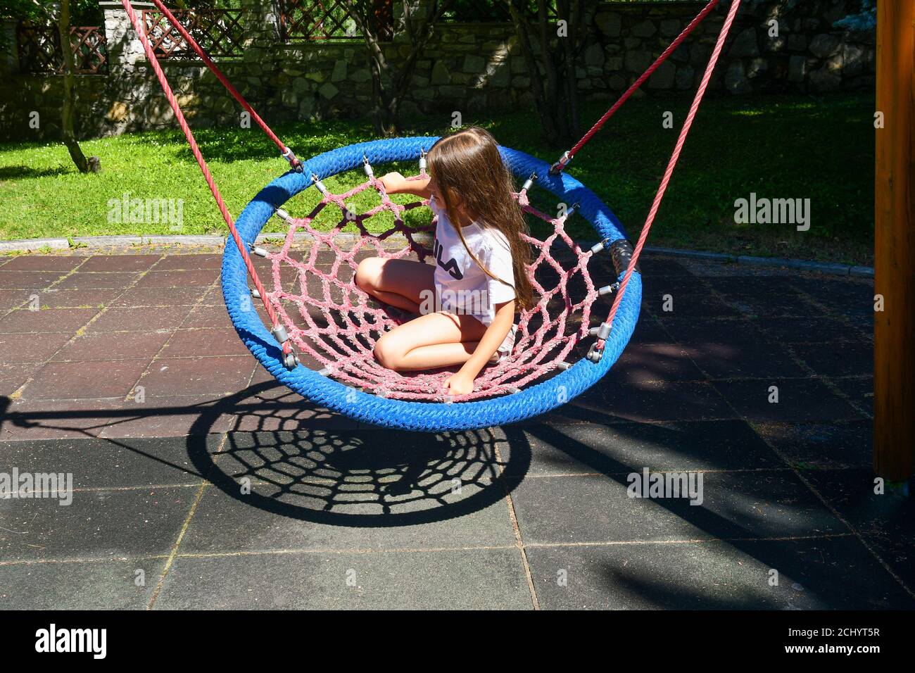 A little girl swinging on a spider web nest swing in a children playground in summer, Courmayeur, Aosta, Aosta Valley, Italy Stock Photo