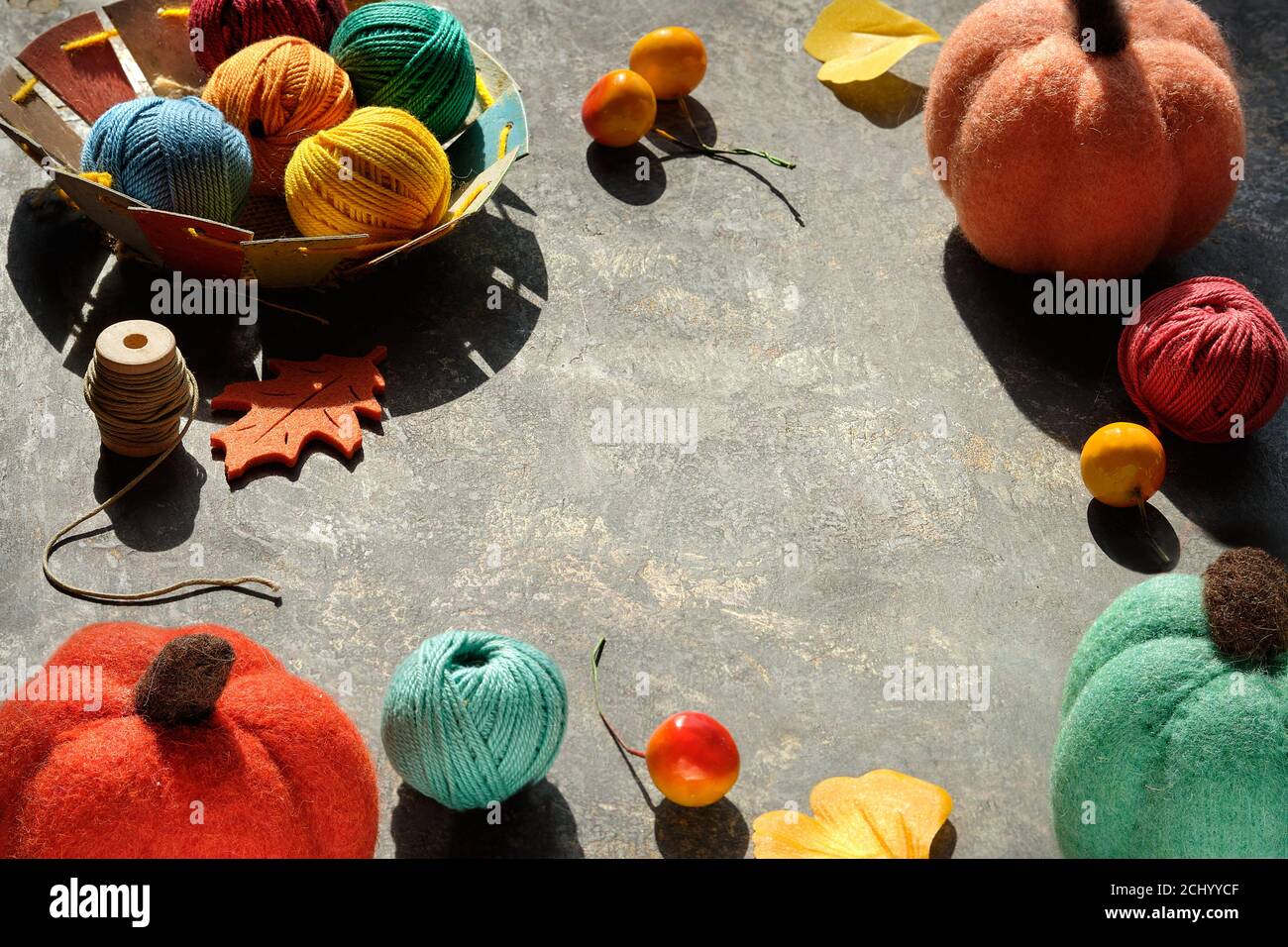 Creative arrangement of craft materials for knitting and crochet with copy-space. Dark table with yarn balls, felt pumpkins, Fall leaves and berry. Stock Photo