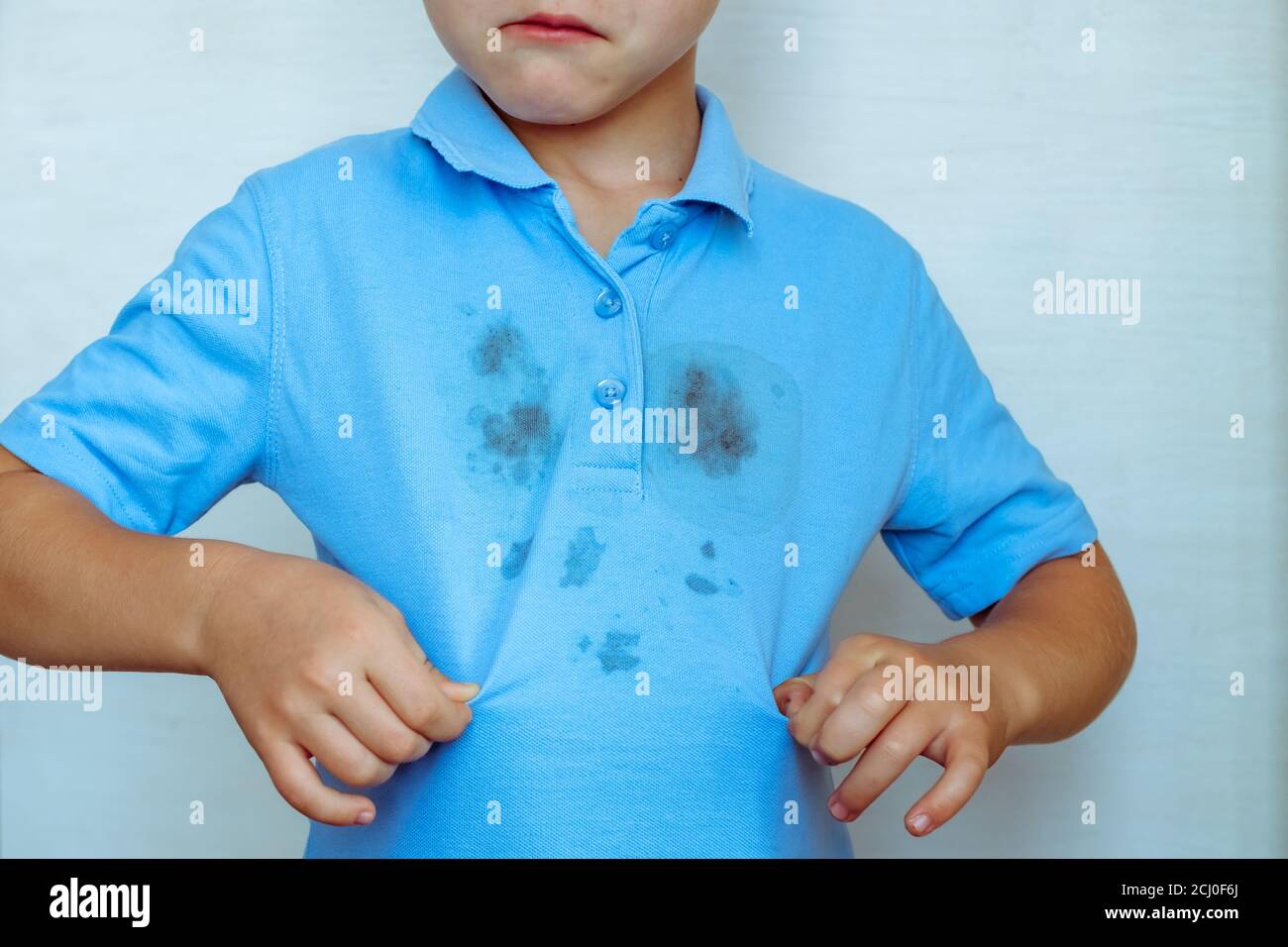 upset boy showing a stain on his clothes The concept of cleaning stains on clothes. Isolated on a white background Stock Photo