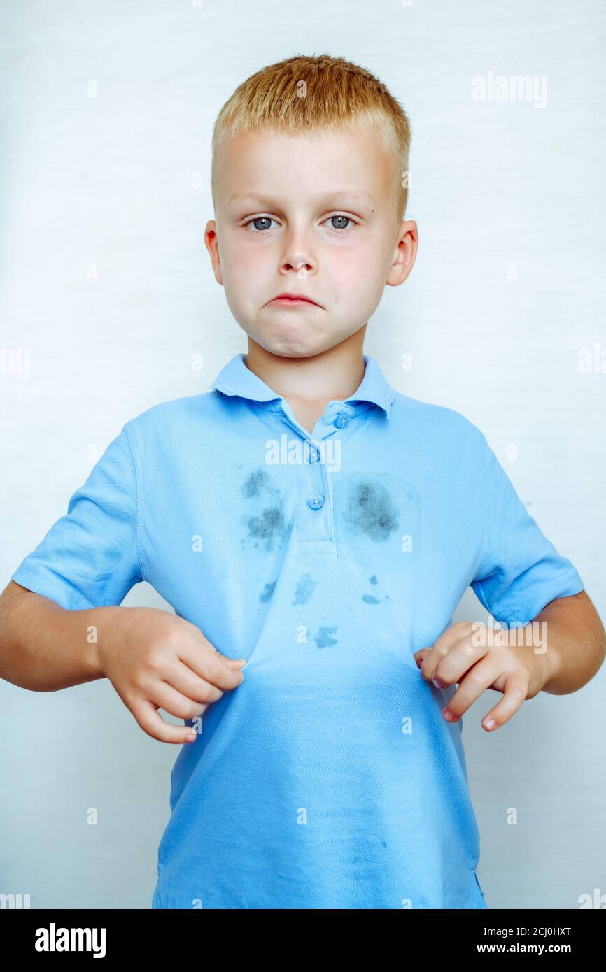 upset boy showing a stain on his clothes The concept of cleaning stains on clothes. Isolated on a white background. High quality photo Stock Photo