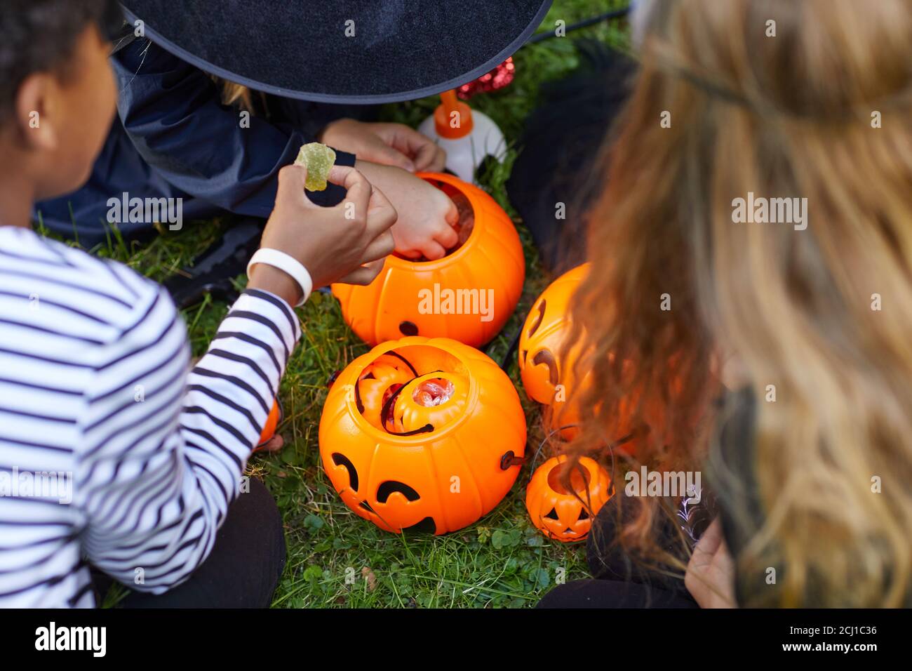 High angle view at group of kids wearing costumes taking candy from Halloween buckets outdoors, copy space Stock Photo