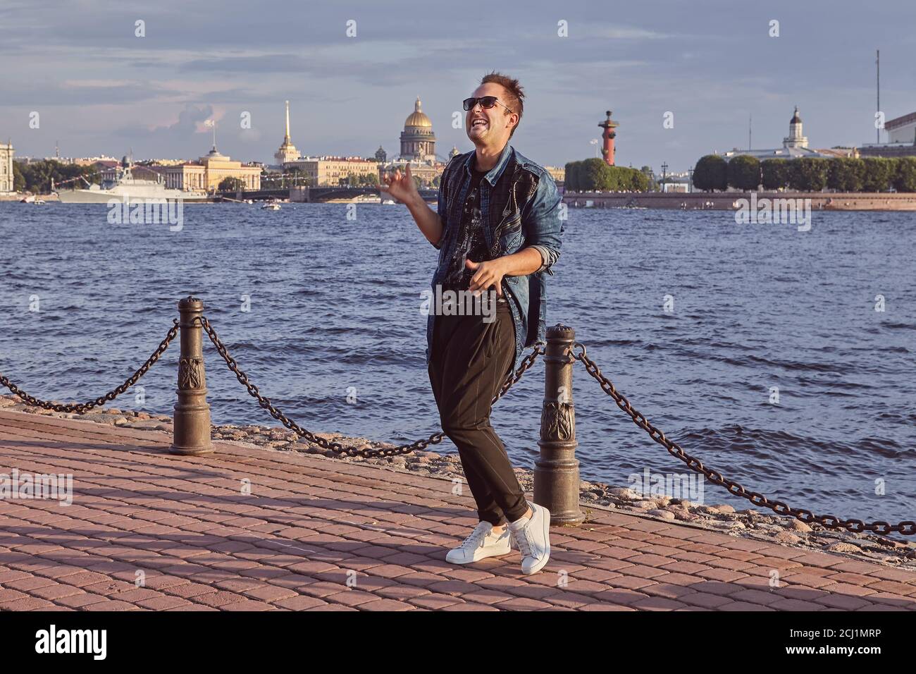Man 20 years old is dancing on the waterfront of Neva river during trip in Saint-Petersburg. Young male is travelling over Russia. Stock Photo