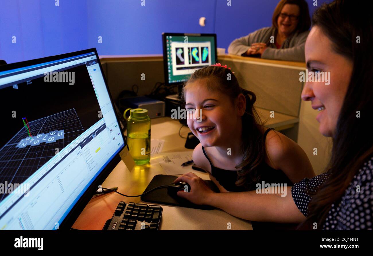 Ryleah Geisner, 8, laughs as she looks at a computer image of herself walking with reflective and surface EMG sensors attached to her body in the Center for Gait and Movement Analysis lab at Children's Hospital Colorado in Aurora, Colorado, U.S., February 9, 2017 with lab engineer Kayla Burnim (R.)  Ryleah has cerebral palsy, a congenital disorder of movement, muscle tone, or posture. The lab was using 3-D motion capture technology to analyze Ryleah's body movement and muscle activity while walking and that data will then be used to formulate a treatment plan for her. In the background is Ryle Stock Photo