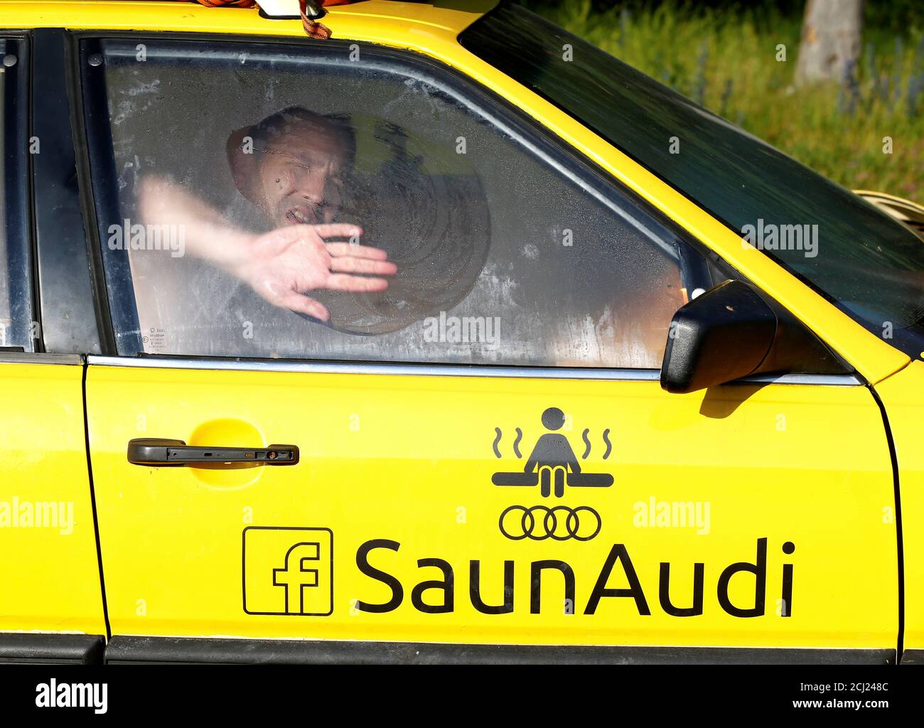 Tauri Liiv cleans a window as he enjoys bathing in an old yellow Audi car  converted
