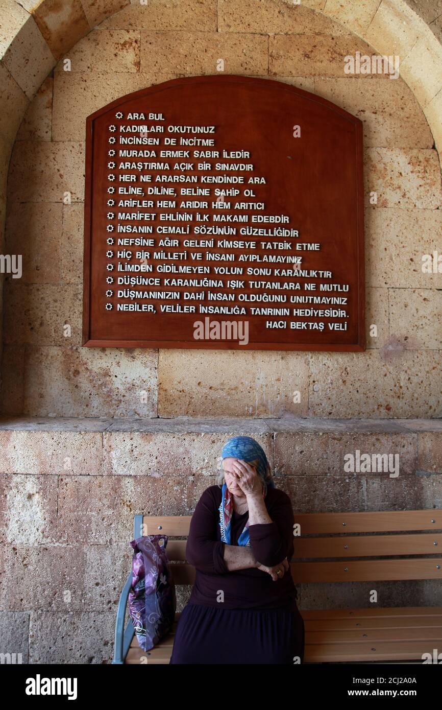 HACI BEKTAS, TURKEY - AUGUST 25: Old woman visiting at famous mosque of Haci Bektas Veli and behind writes the rules of humanity on August 25, 2013 in Nevsehir, Turkey. Stock Photo
