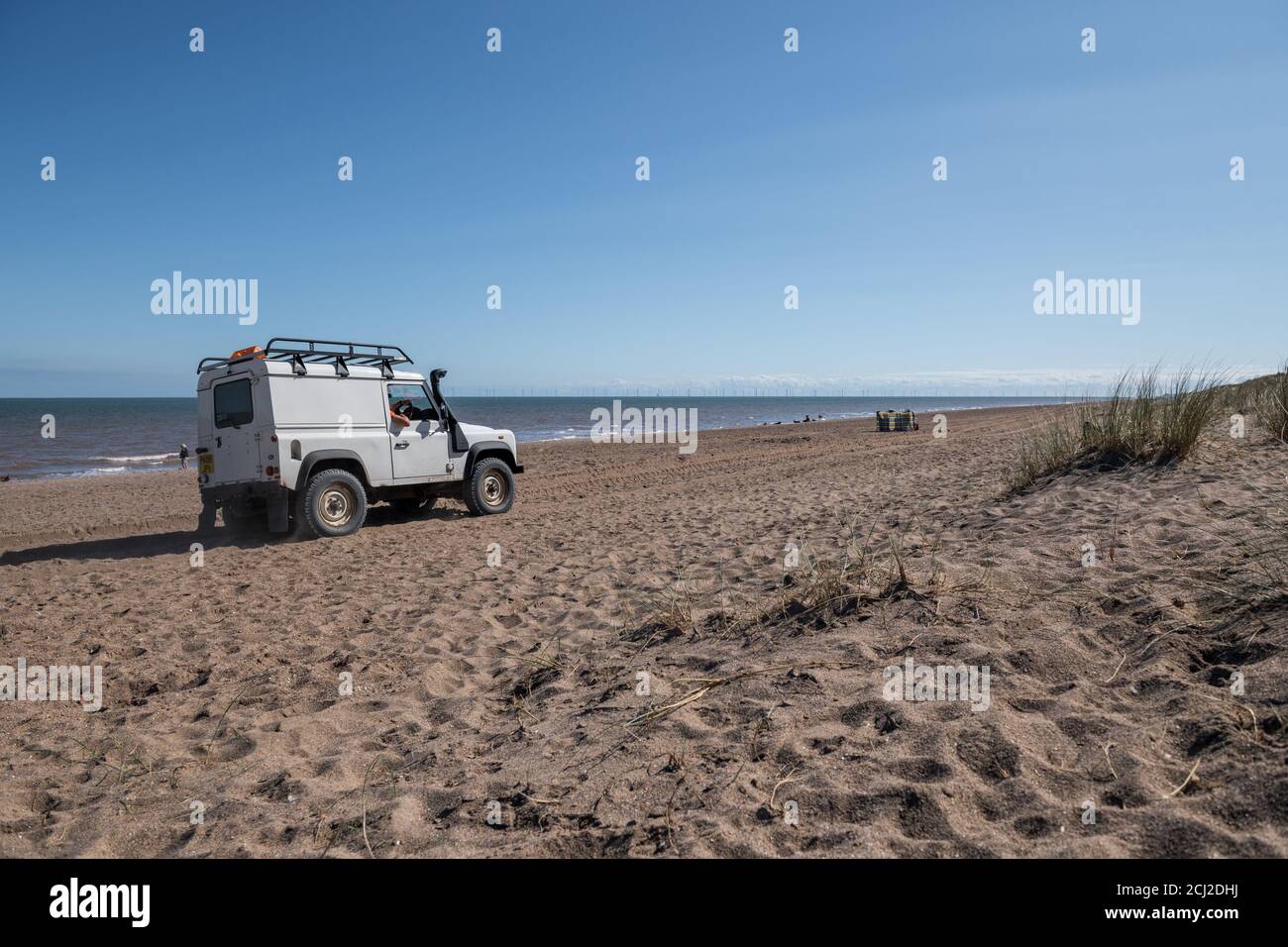 Grey beach patrol Land Rover 90 station wagen being driven along the sandy beach by Anderby, on the Linclonshire coast line, England. Stock Photo