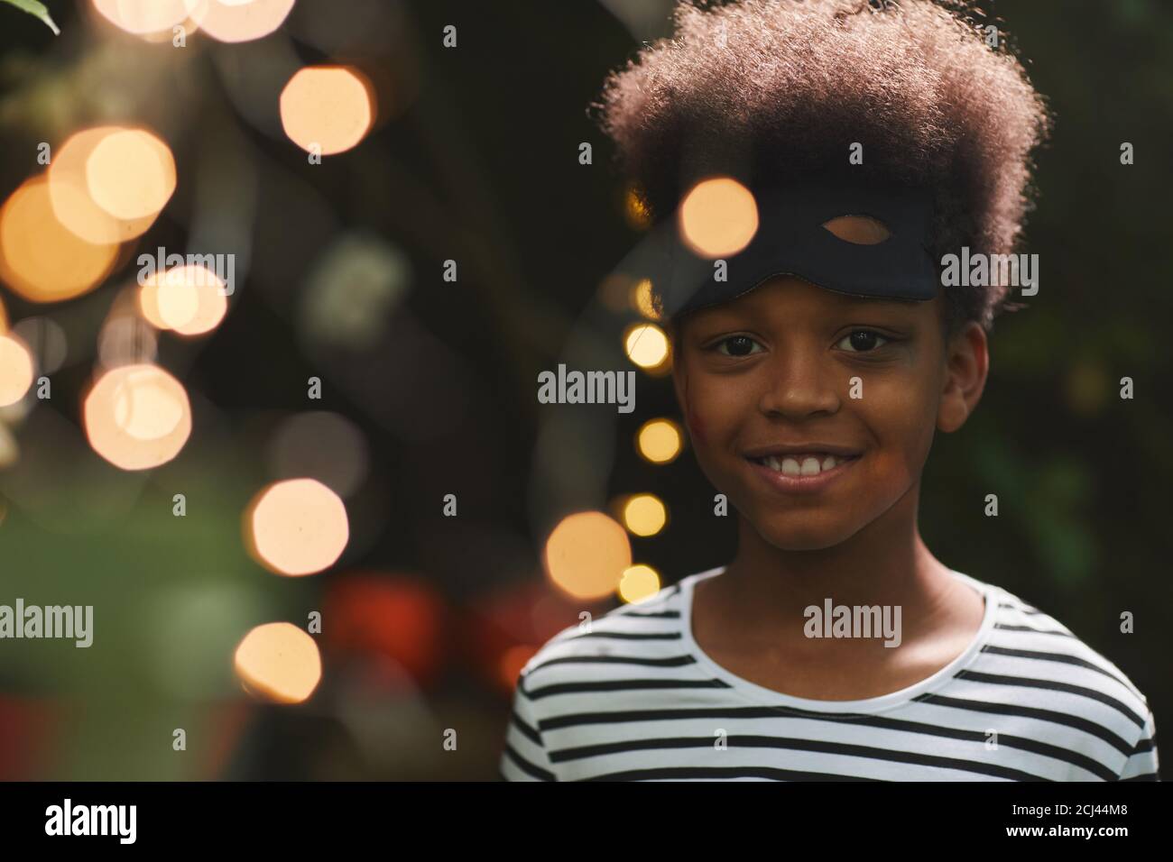 Portrait of smiling African-American boy looking at camera during outdoor Halloween party with lights , copy space Stock Photo