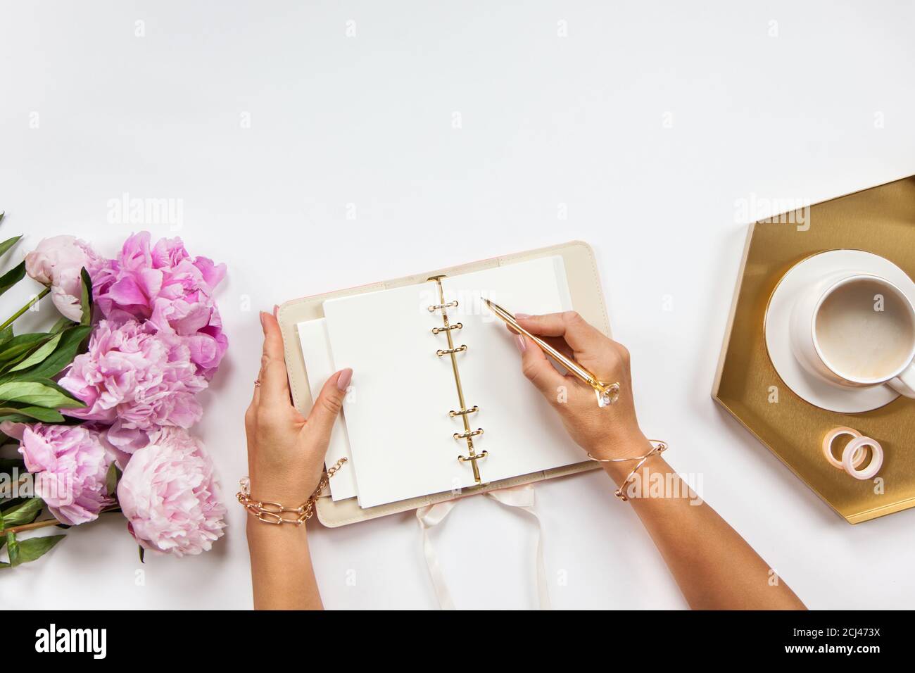 Well-groomed woman hands is writing in diary with stationery supplies set onside and peonies bouquet Stock Photo