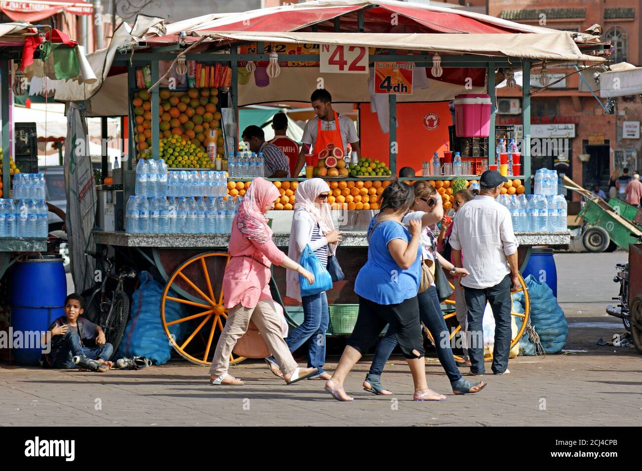 A fruit and juice stand is passed by people during the day in the Marrakech old medina market in Marrakech, Morocco. Stock Photo