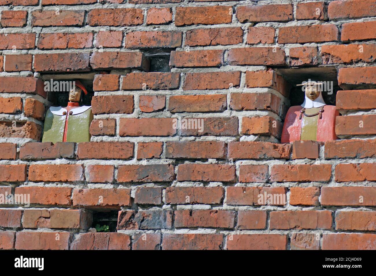 Teutonic Order townspeople figures seemingly look out holes in the brick wall located in the old town of Torun, Poland. Stock Photo