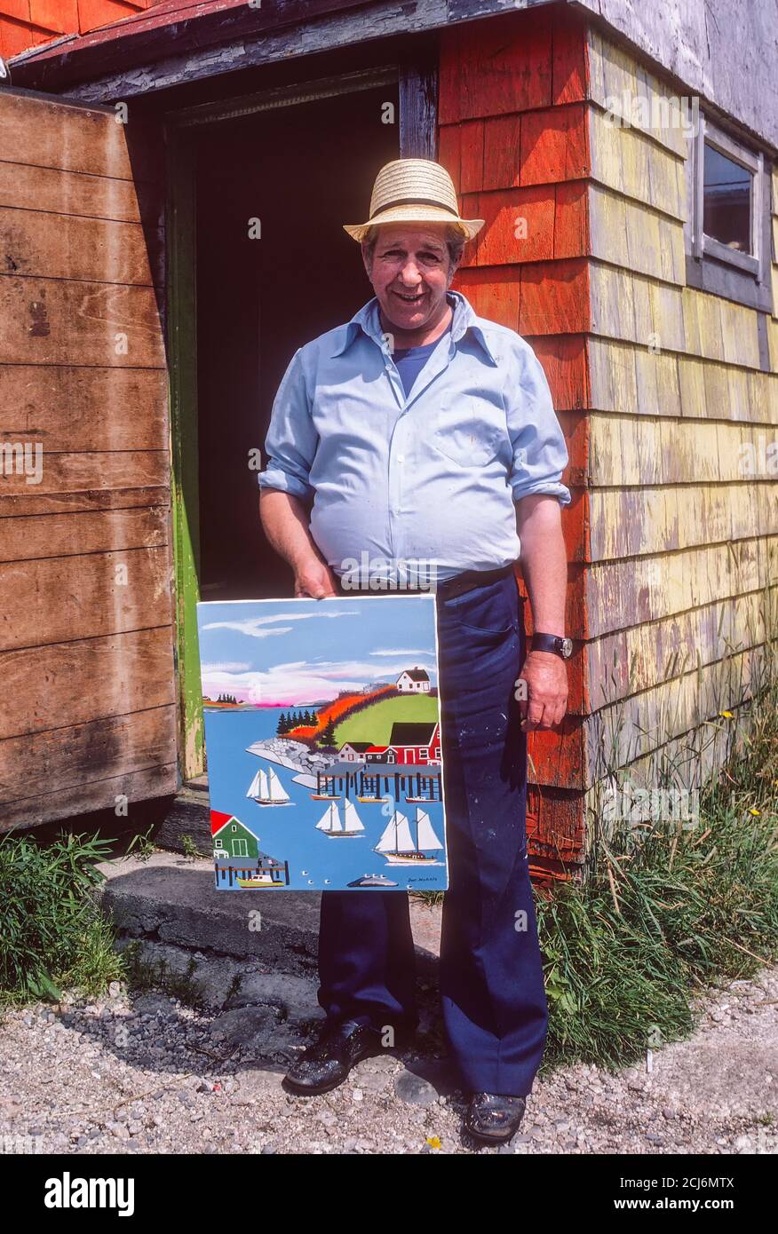 Joe Norris (1924-1996), Nova Scotia folk artist, holding one of his paintings while standing in front of his home. Stock Photo