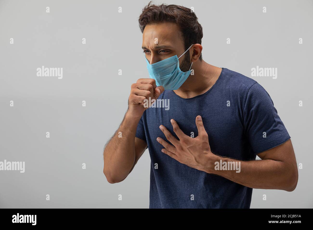 Young man coughing wearing a mask with his hand on chest Stock Photo