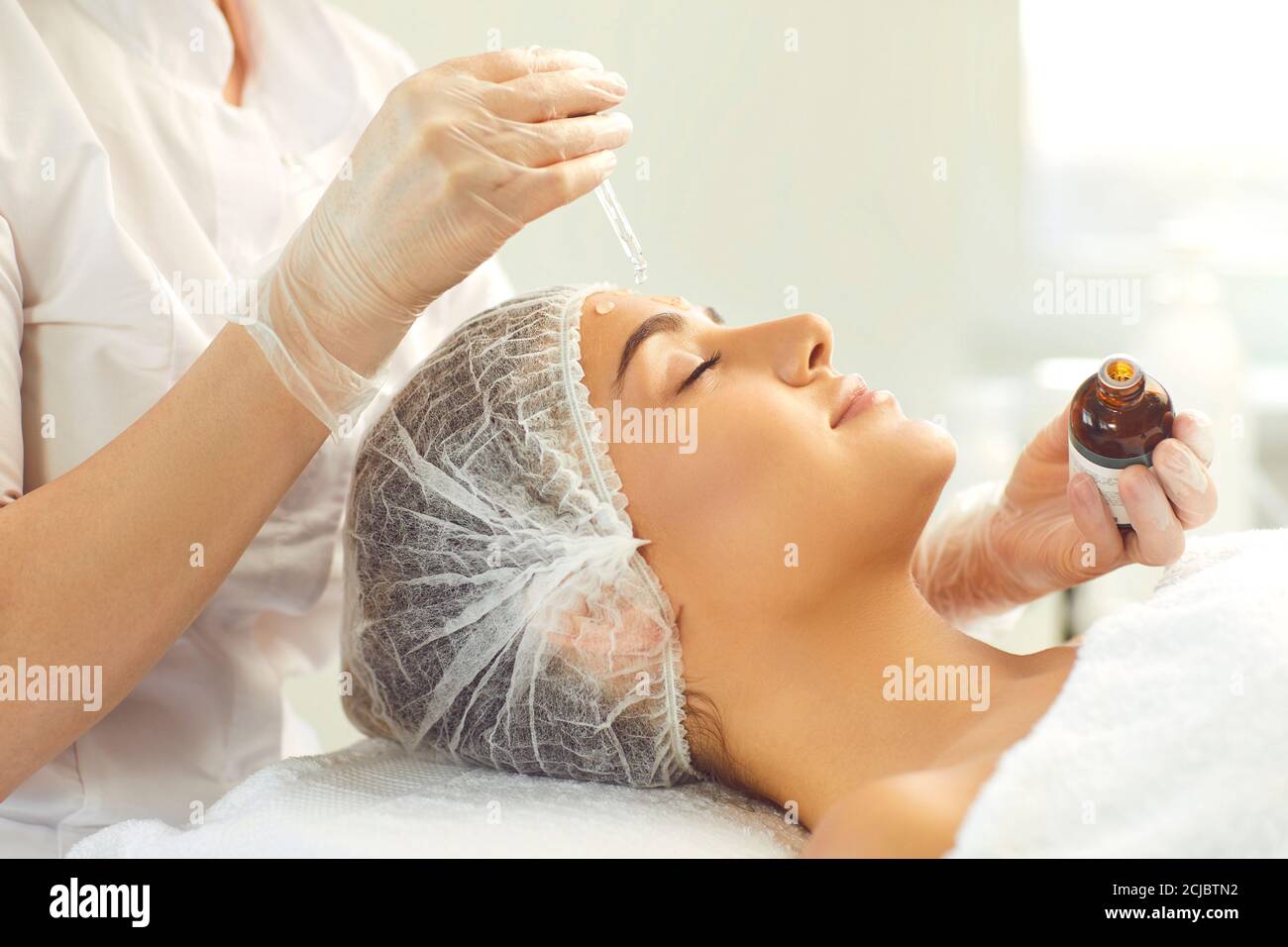 Professional cosmetician using pipette to apply moisturizing serum on client's face Stock Photo