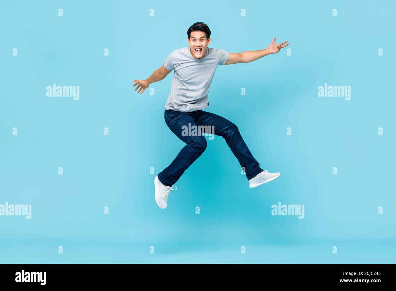 Energetic happy young Asian man in casual clothes jumping studio shot isolated in light blue background Stock Photo