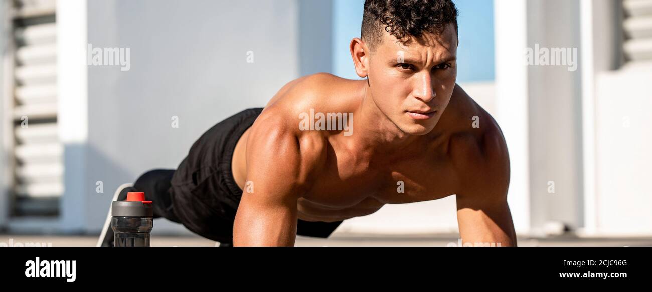 Banner image of handsome muscular sports man doing plank exercise outdoors on rooftop Stock Photo
