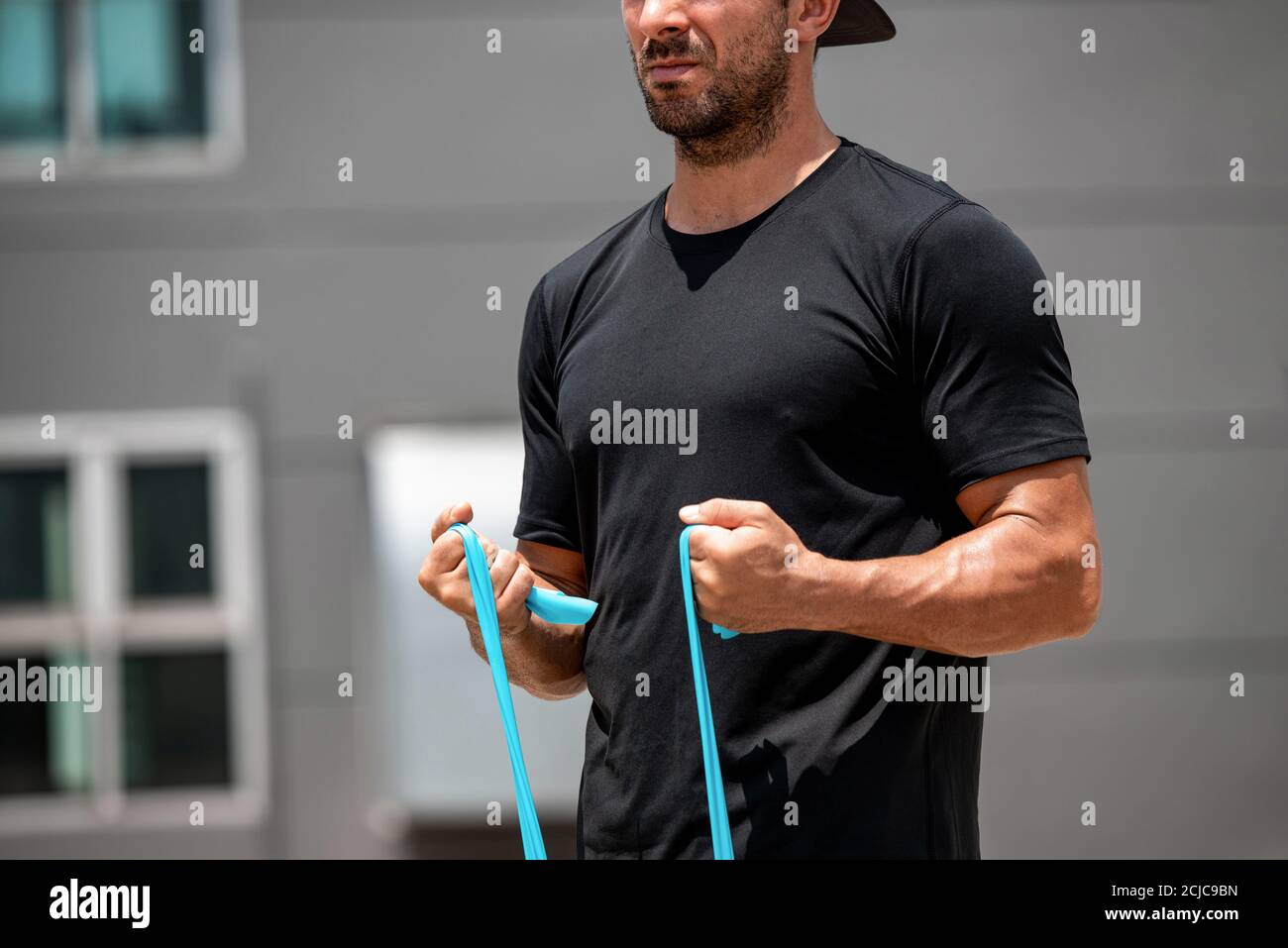 Fit muscular sports man doing bicep curl exercise with resistance band at home in the open air Stock Photo