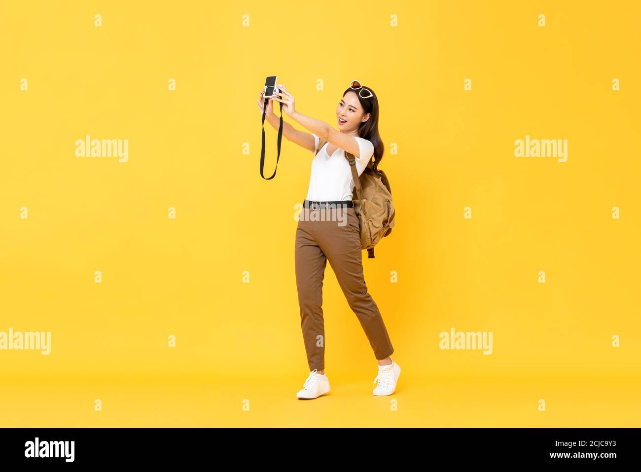 Young pretty Asian tourist girl taking selfie with digital camera in yellow isolated background Stock Photo