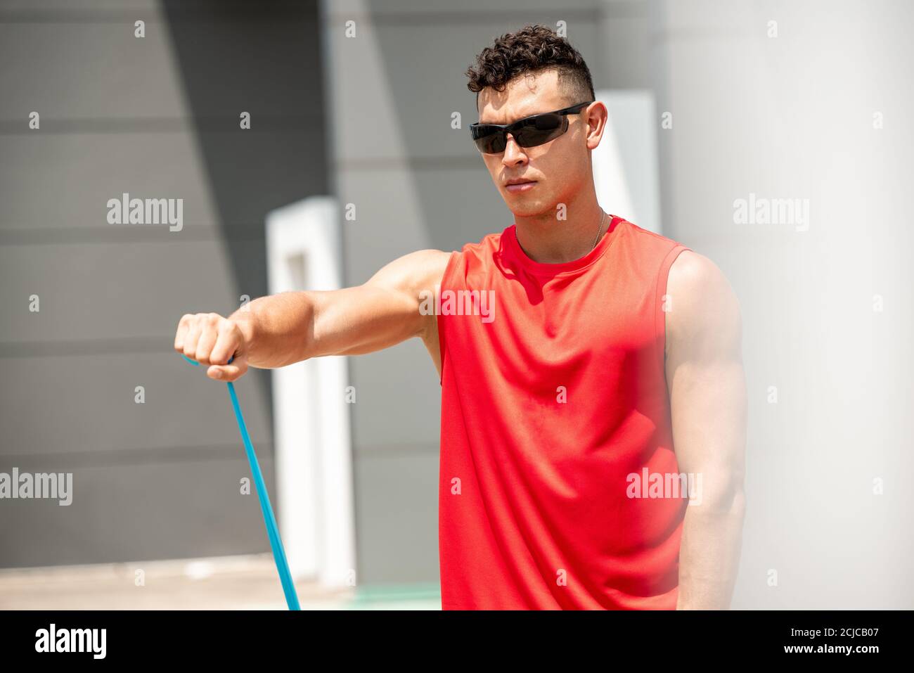 Handsome sports man doing shoulder front raise exercise with elastic resistance band outdoors - home open air workout concept Stock Photo