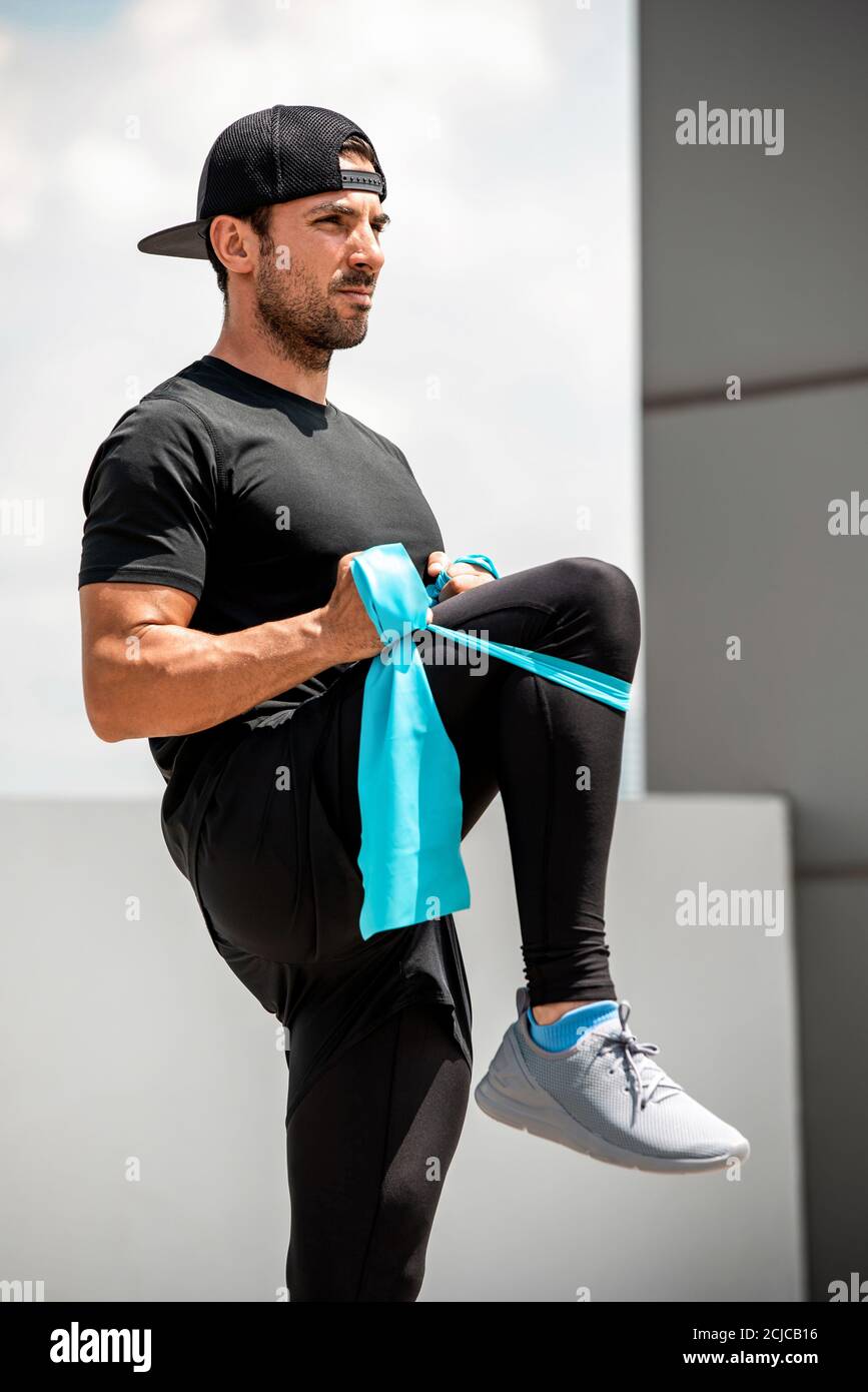 Handsome Hispanic man warming up with elastic resistance band before exercise outdoors at rooftop - home open air work out concept Stock Photo