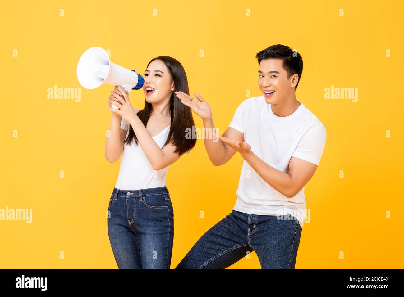 Cheerful portrait of smiling happy young Asian couple making announcement and presenting in isolated studio yellow background Stock Photo