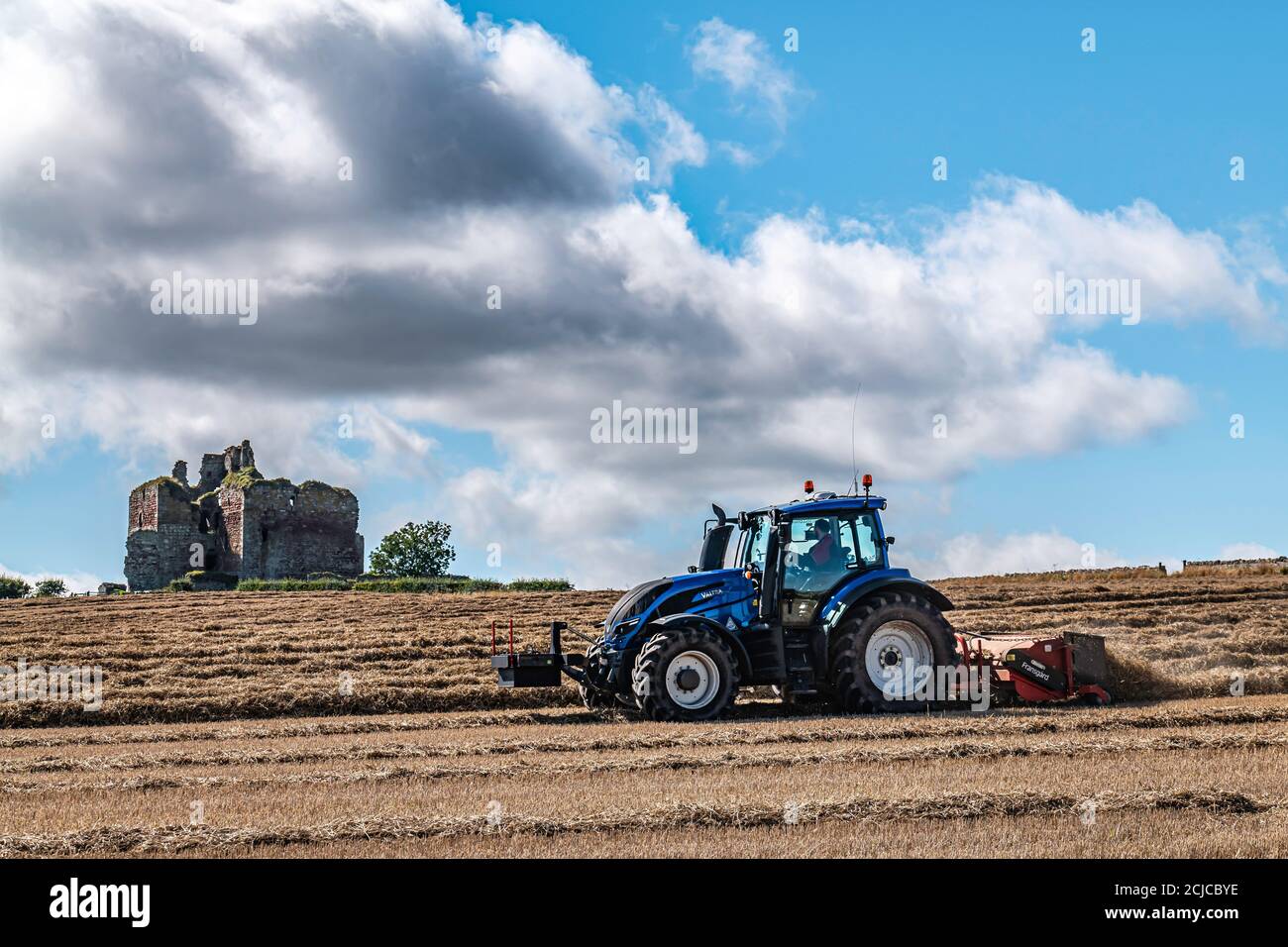 Cessford, Kelso, Scottish Borders, Scotland, UK. 8th September 2020. A farmer prepares straw for baling against the backdrop of Cessford Castle near K Stock Photo