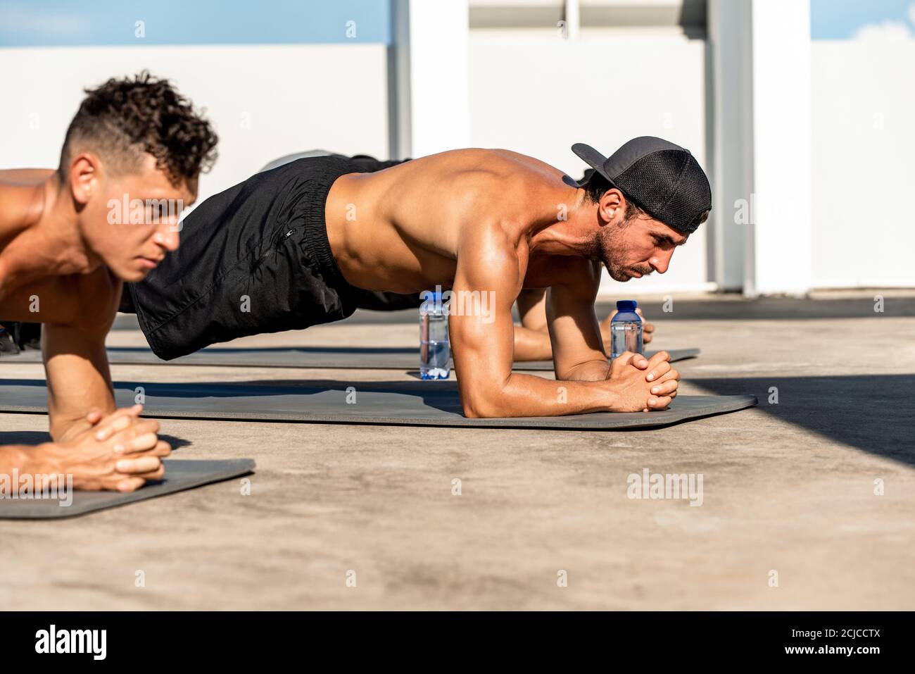 Group of athletic men doing plank morning workout exercise outdoors on rooftop floor Stock Photo