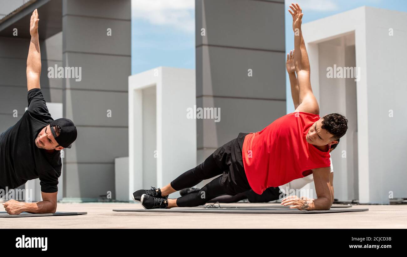 Group of athletic men doing side plank morning workout exercise outdoors on rooftop floor Stock Photo