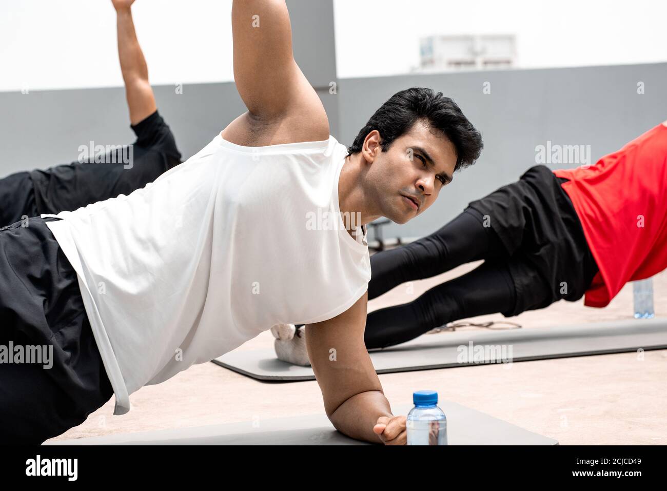 Group of athletic men doing side plank morning workout exercise outdoors on rooftop floor Stock Photo