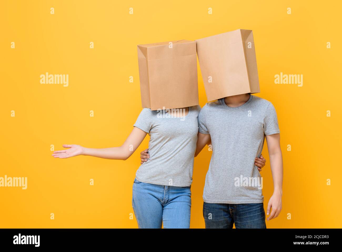 Conceptual protrait of anonymous covered face couple holding each other doing open palm gesture isolated on yellow studio background Stock Photo