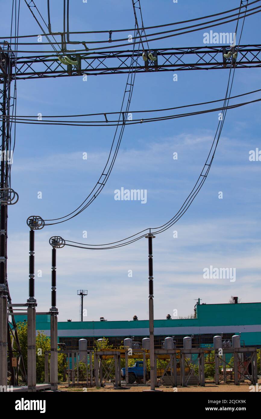 Electric power station. Transformer station (electrical substation). Wires and insulators (isolators) and green industrial building on blue sky bckgd. Stock Photo