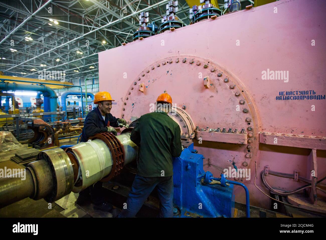 Electric power station. Two workers fixing  pink electric machine generator in factory workshop. Stock Photo