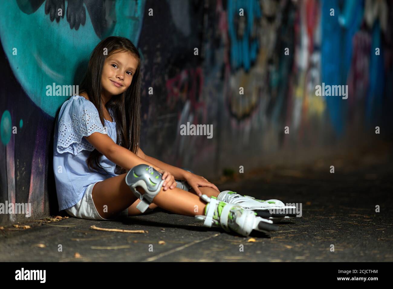happy tired little child girl in roller skates is sitting after rollerskating in park in the