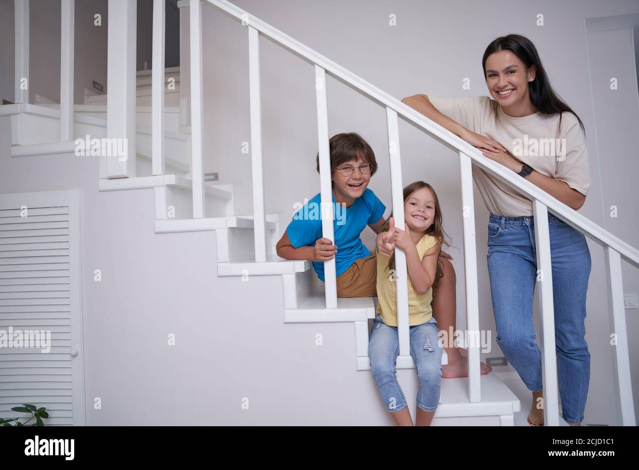 Positive young mother and her two cute little kids looking at camera ...