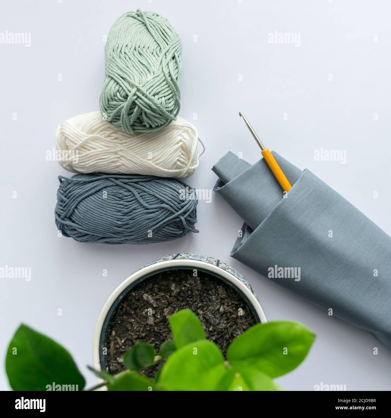 Three Pastel colored Balls of Yarn with crochet hook and cotton fabric, flat lay Stock Photo