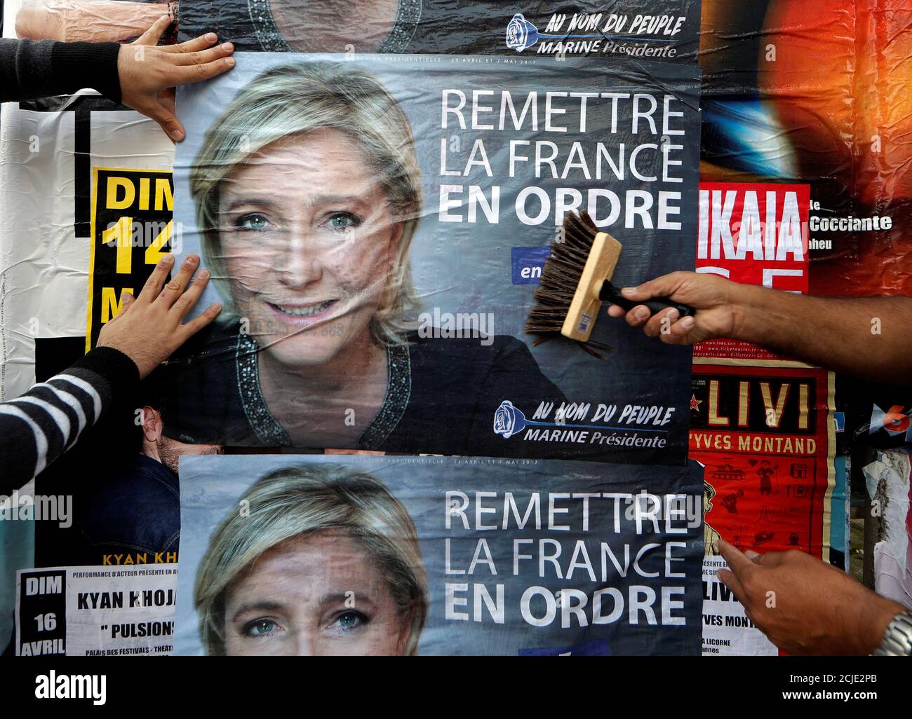 Members of the French National Front (FN) political party paste a poster on  a free billboard for French National Front (FN) political party leader  Marine Le Pen as part of the 2017