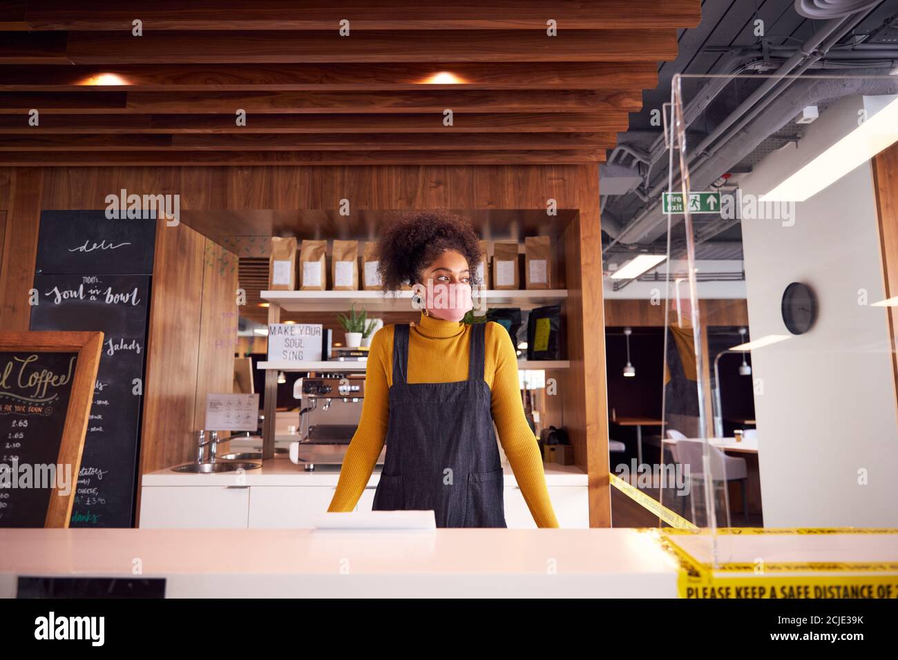 Female Small Business Owner Of Coffee Shop In Mask Standing Behind Counter During Health Pandemic Stock Photo