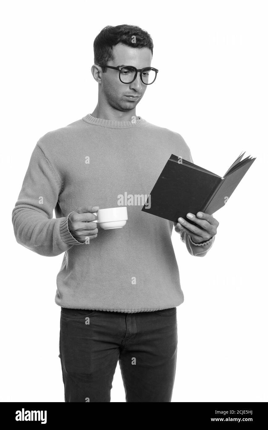 Young handsome Iranian man reading book while holding coffee cup Stock Photo
