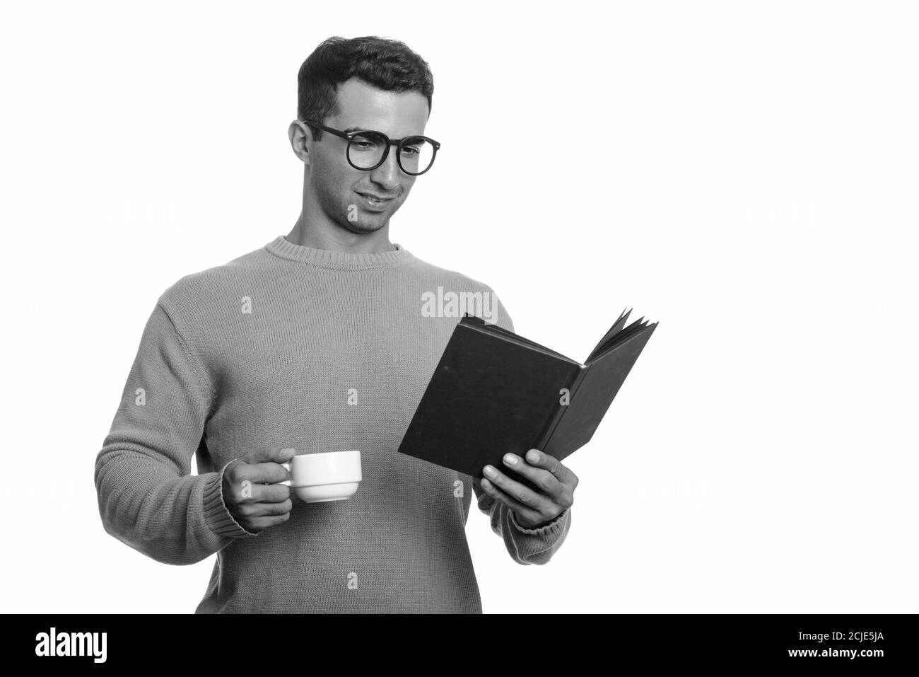 Young happy Iranian man reading book while holding coffee cup Stock Photo
